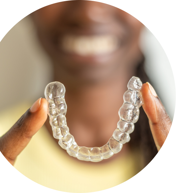 African American woman holding invisalign clear retainer between two fingers, upwards, making a smile shape.