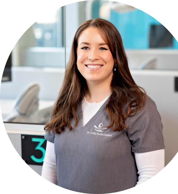 Orthodontist, Dr. Emily Koufos Radford smiling in her gray orthodontic scrubs