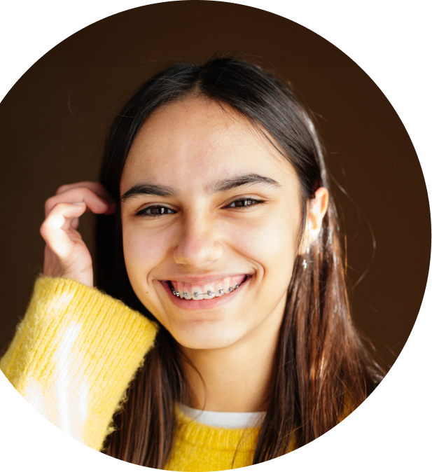 Teenager with braces smiling in a yellow sweater while tucking her hair behind her ear